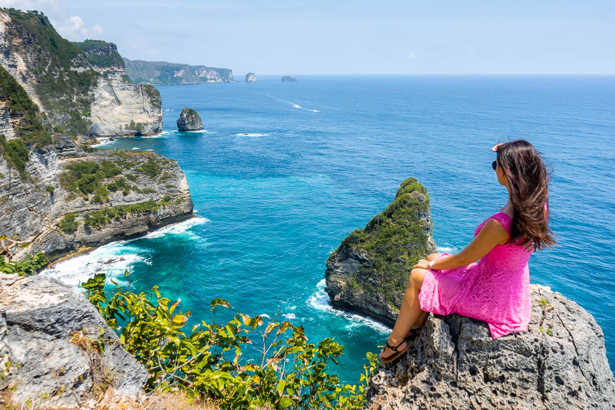 Girl in a pink dress sitting on a cliff, looking at the view at Banah Cliff Point, Nusa Penida