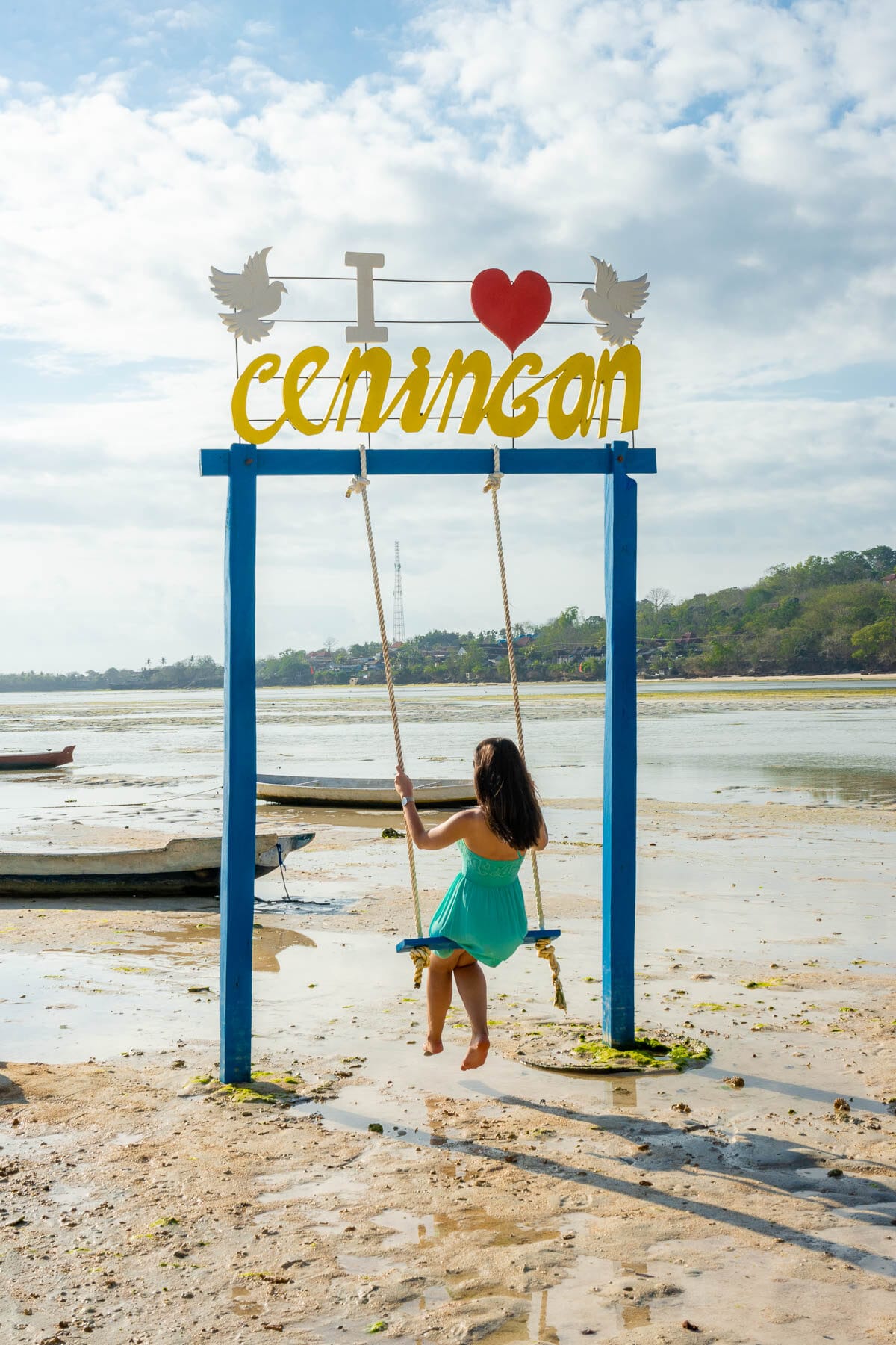 Girl in a blue dress sitting on a swing at a beach on Nusa Ceningan