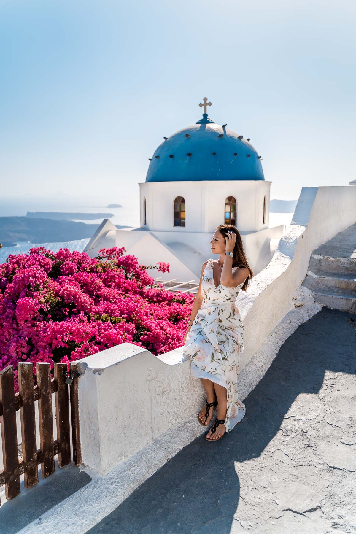 Girl in a floral dress sitting in front of a blue domed church in Imerovigli, Santorini