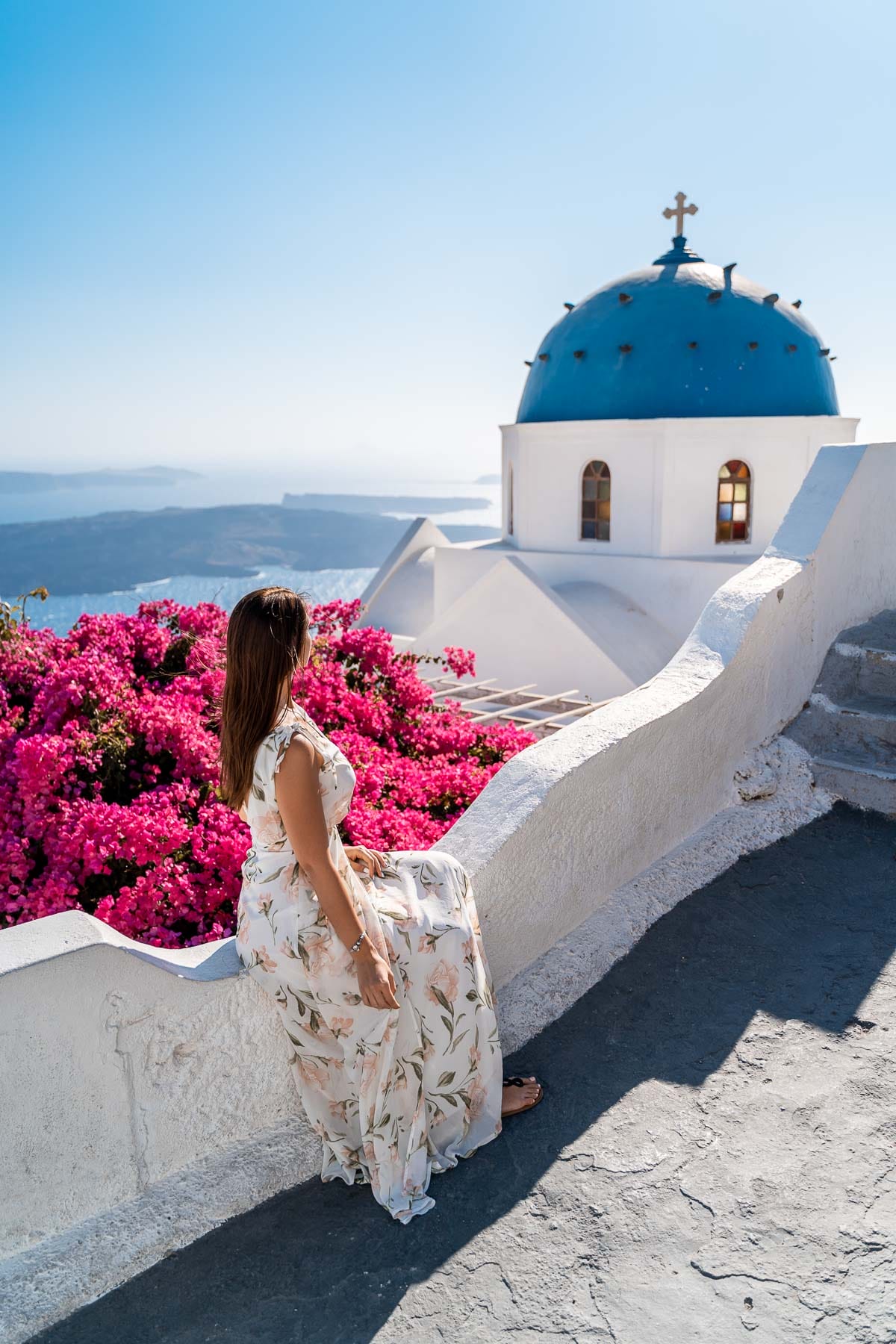 Girl in a floral dress sitting in front of a blue domed church in Imerovigli, Santorini
