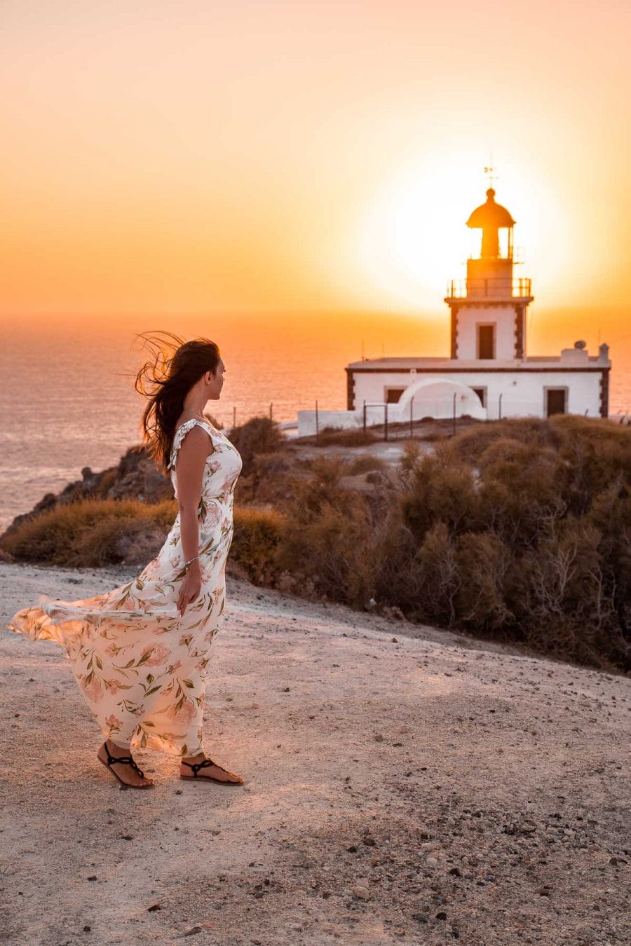 Girl in a floral dress watching the sunset at the Akrotiri Lighthouse in Santorini