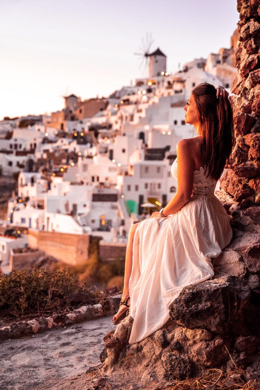 Girl in a white dress sitting in a cave, watching the sunset in Oia, Santorini