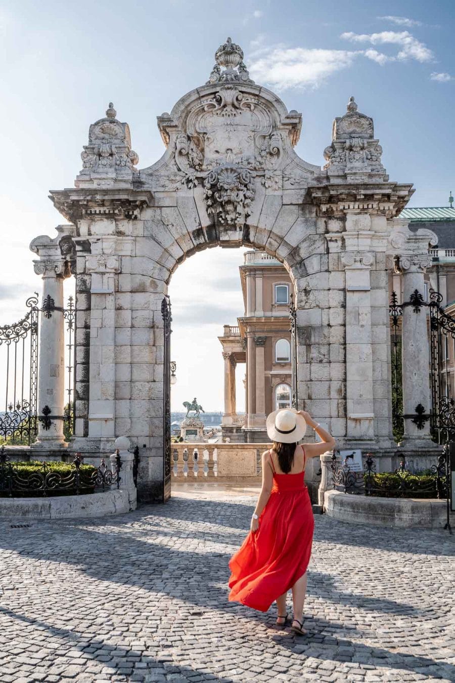 Girl in a red dress and a straw hat standing in front of the Buda Castle
