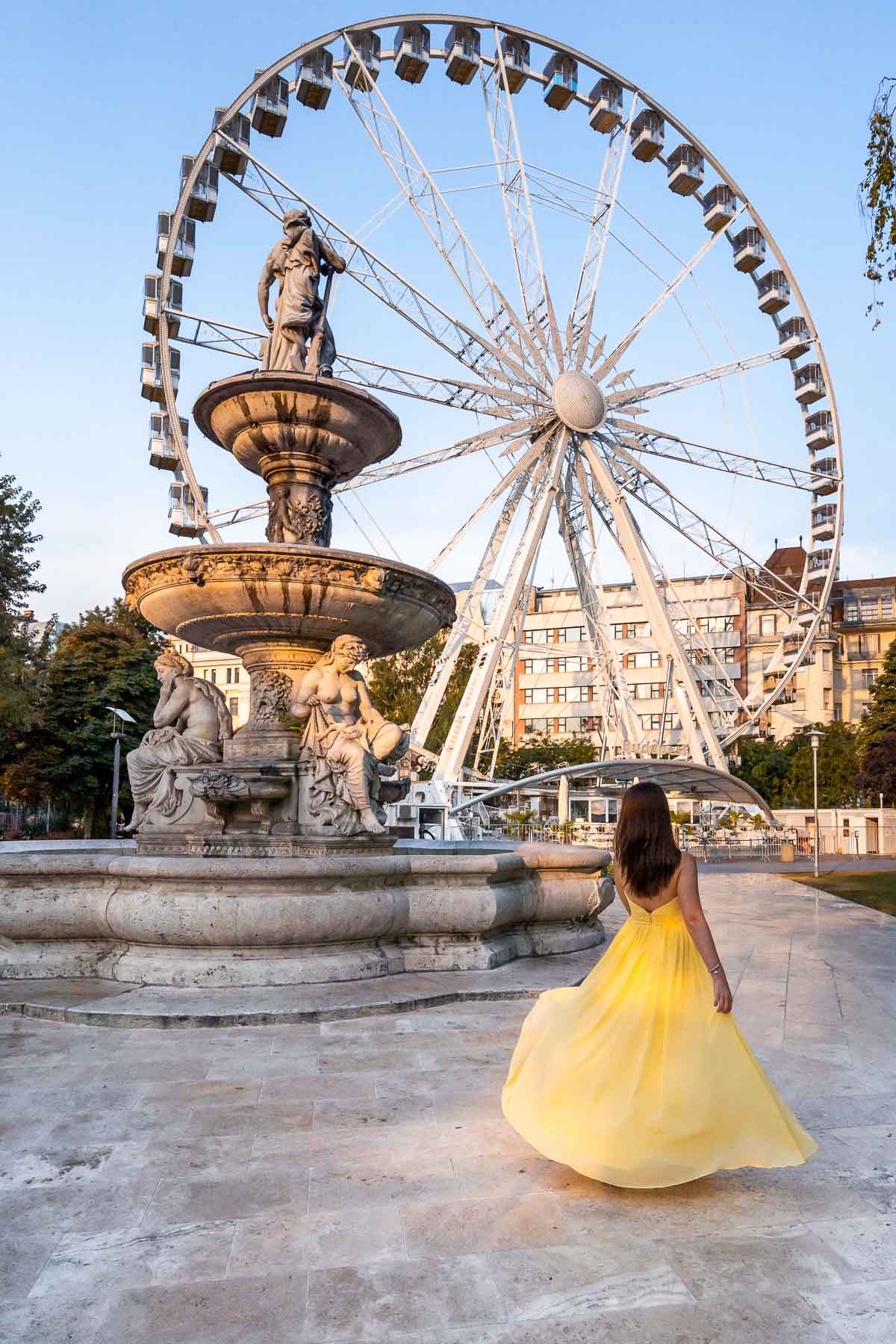 Girl in a yellow dress twirling in front of the Budapest Eye