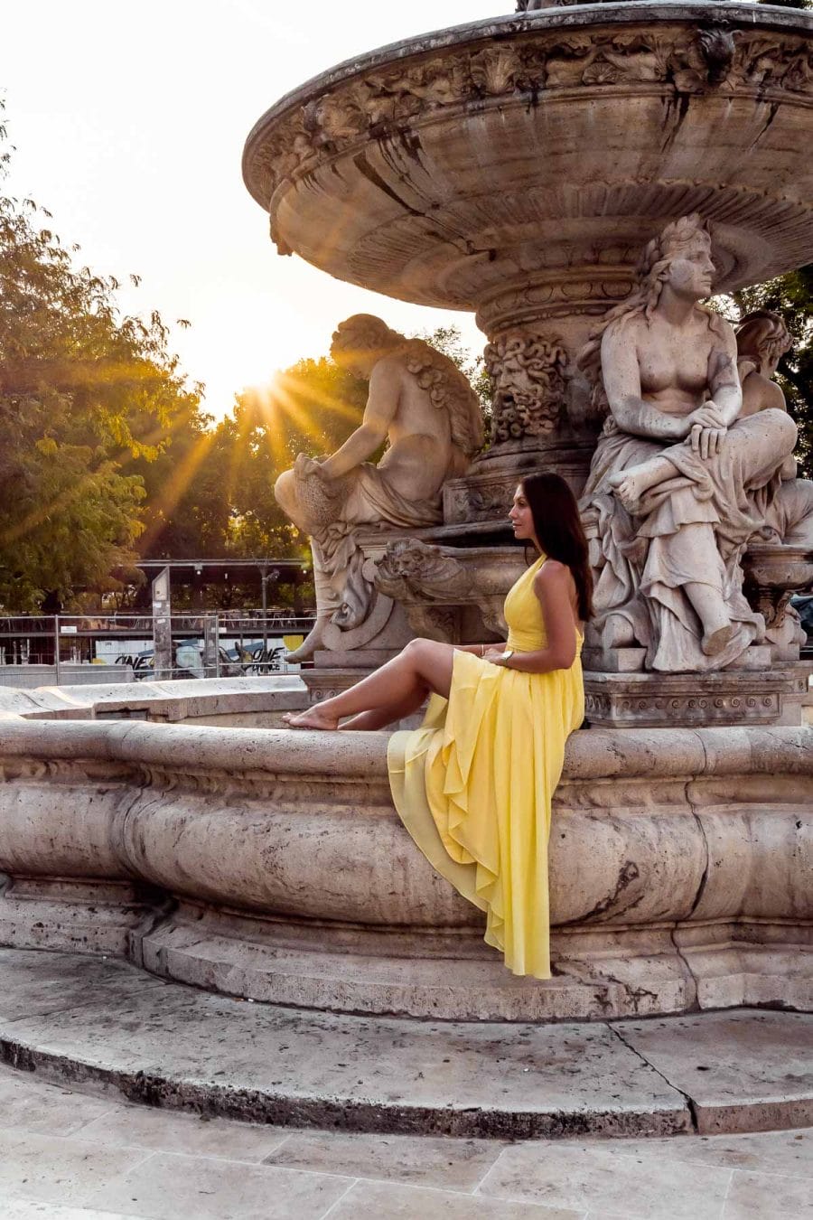 Girl in a yellow dress sitting on the Danubius Fountain in Budapest