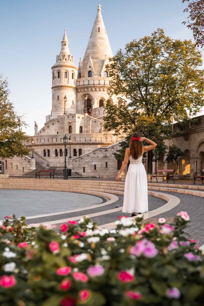 Girl in white dress standing in front of the Fisherman's Bastion in Budapest with colorful flowers in the foreground