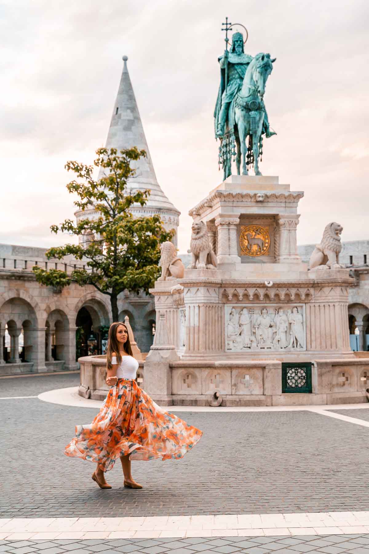 Girl in an orange skirt twirling in front of a statue at Fisherman's Bastion in Budapest