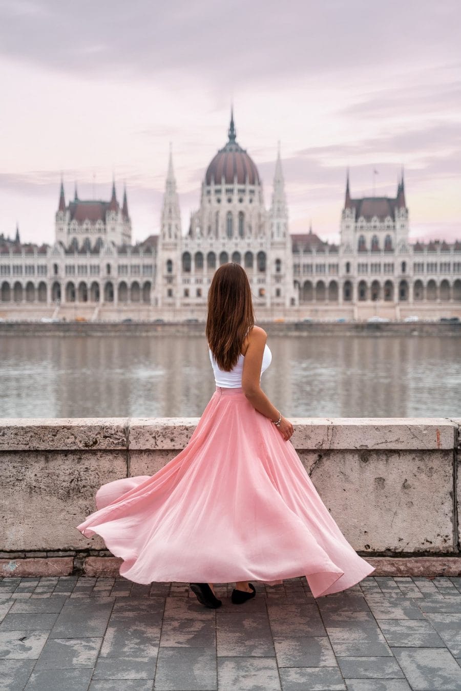 Girl in a pink skirt twirling in front of the Hungarian Parliament at one of the best Budapest Instagram Spots