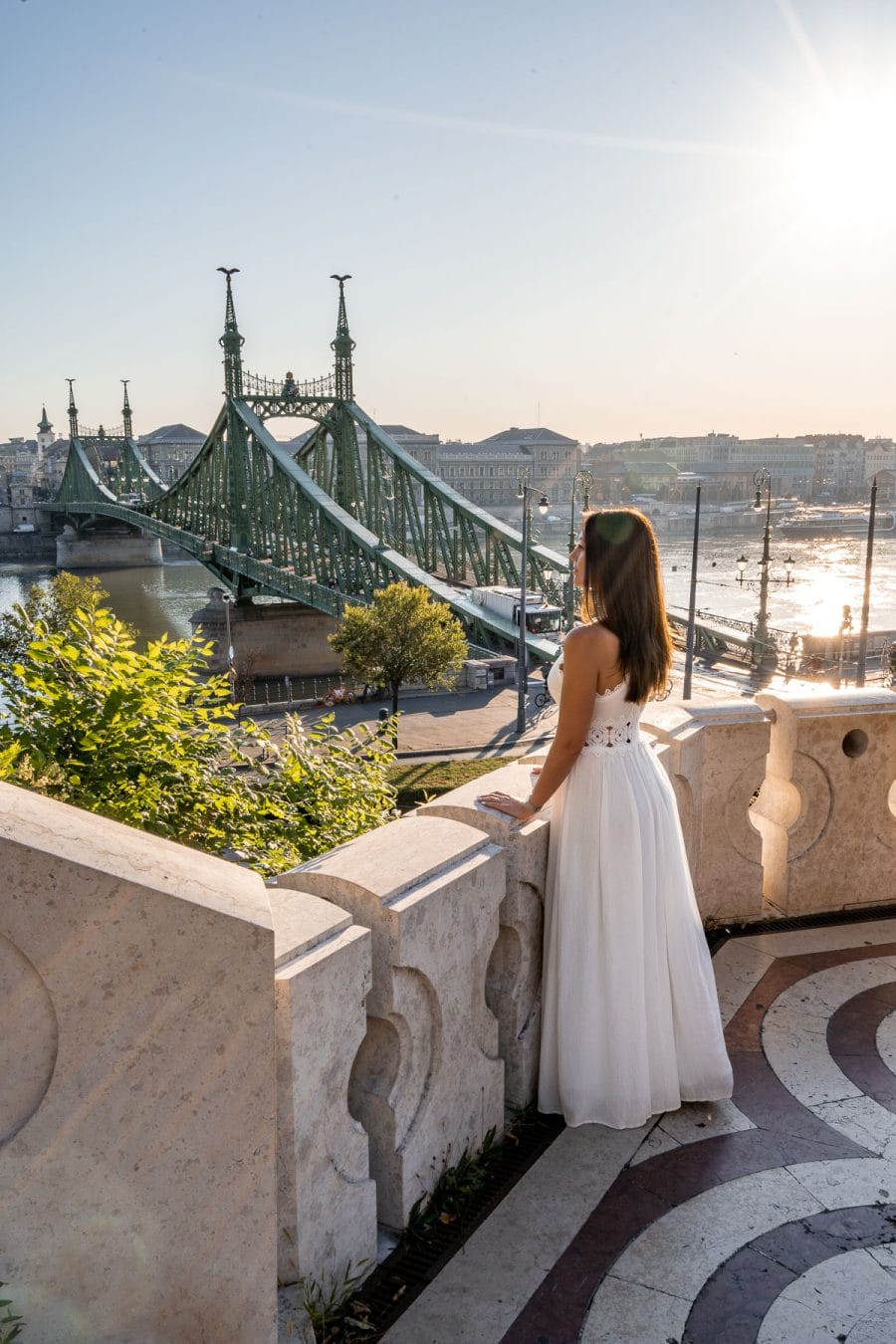 Girl in a white dress standing in front of the Gellért Hill Cave, looking down at the Liberty Bridge in Budapest