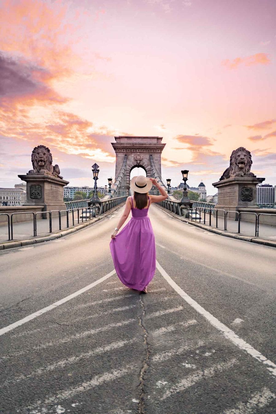 Girl in a purple dress standing in front of the Szechenyi Chain Bridge during sunrise in Budapest