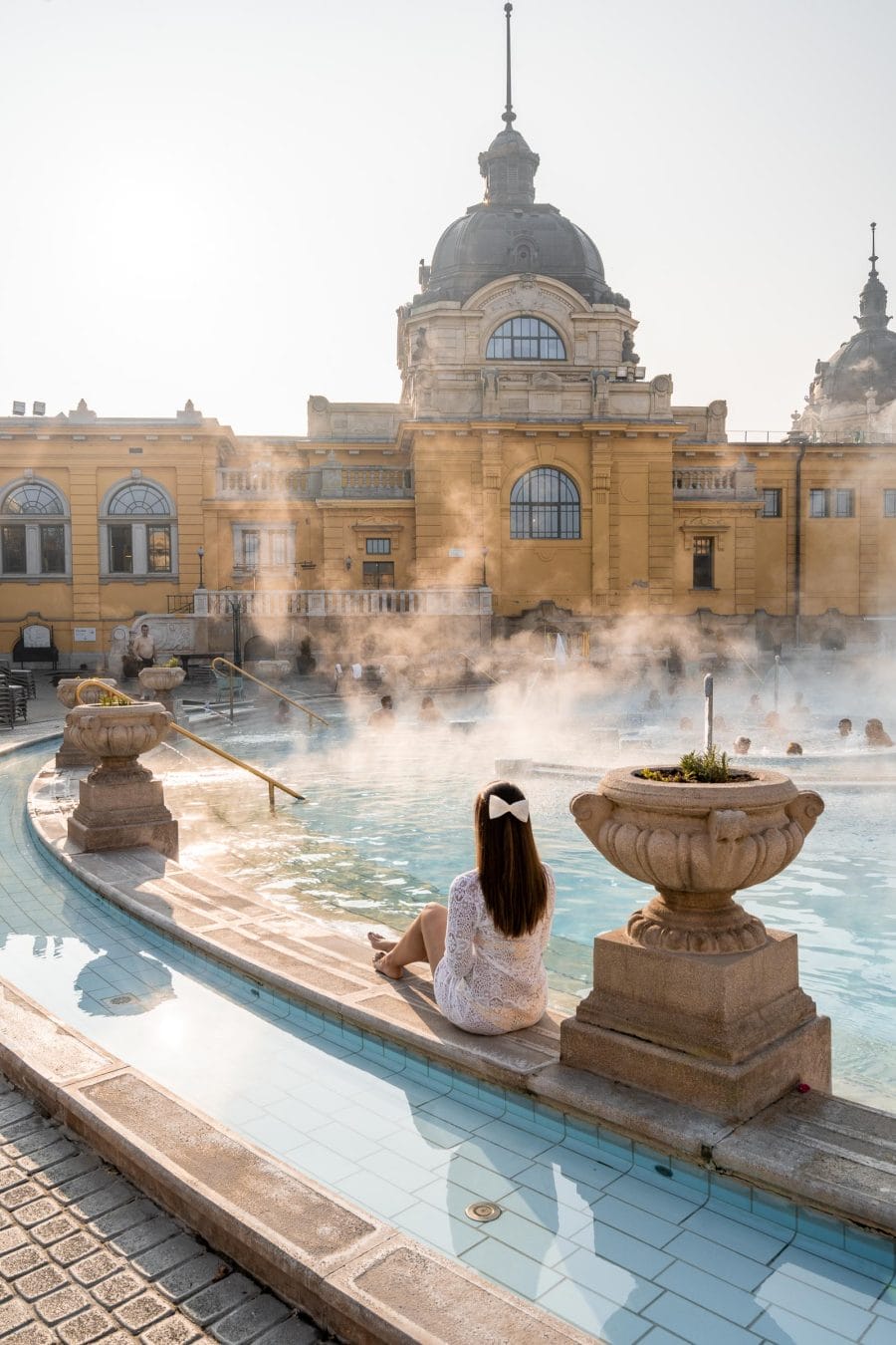 Girl in a white dress sitting at the edge of the pool in the Szechenyi Thermal Bath in Budapest
