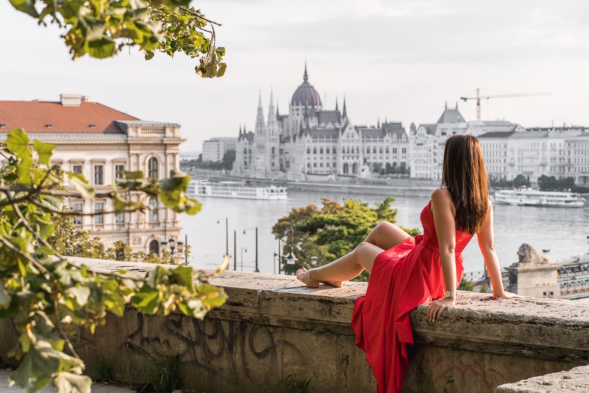 Girl in a red dress sitting on a wall with the Hungarian Parliament in the background