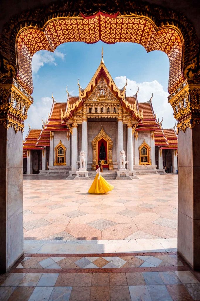 Girl in a yellow dress twirling in front of the Wat Benchamabophit in Bangkok