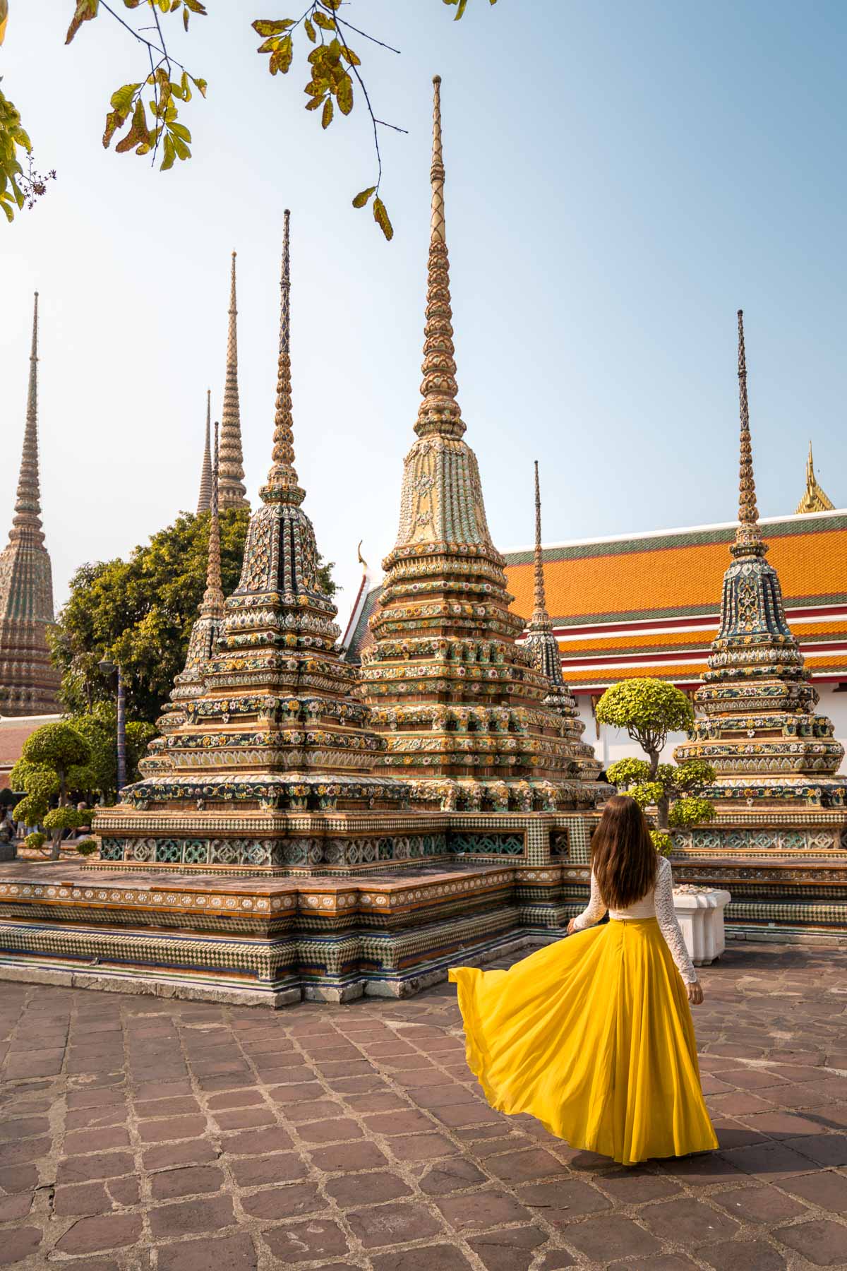Girl in a yellow dress standing in front of the beautifully decorated stupas at the Wat Pho in Bangkok