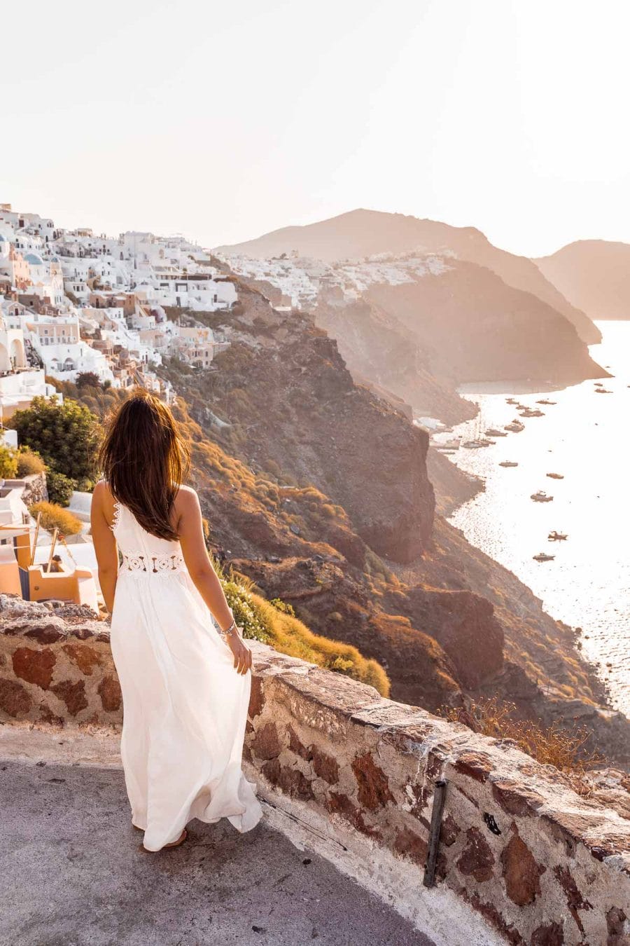 Girl in a white dress standing in the Oia Castle, looking at the view of the caldera at sunrise