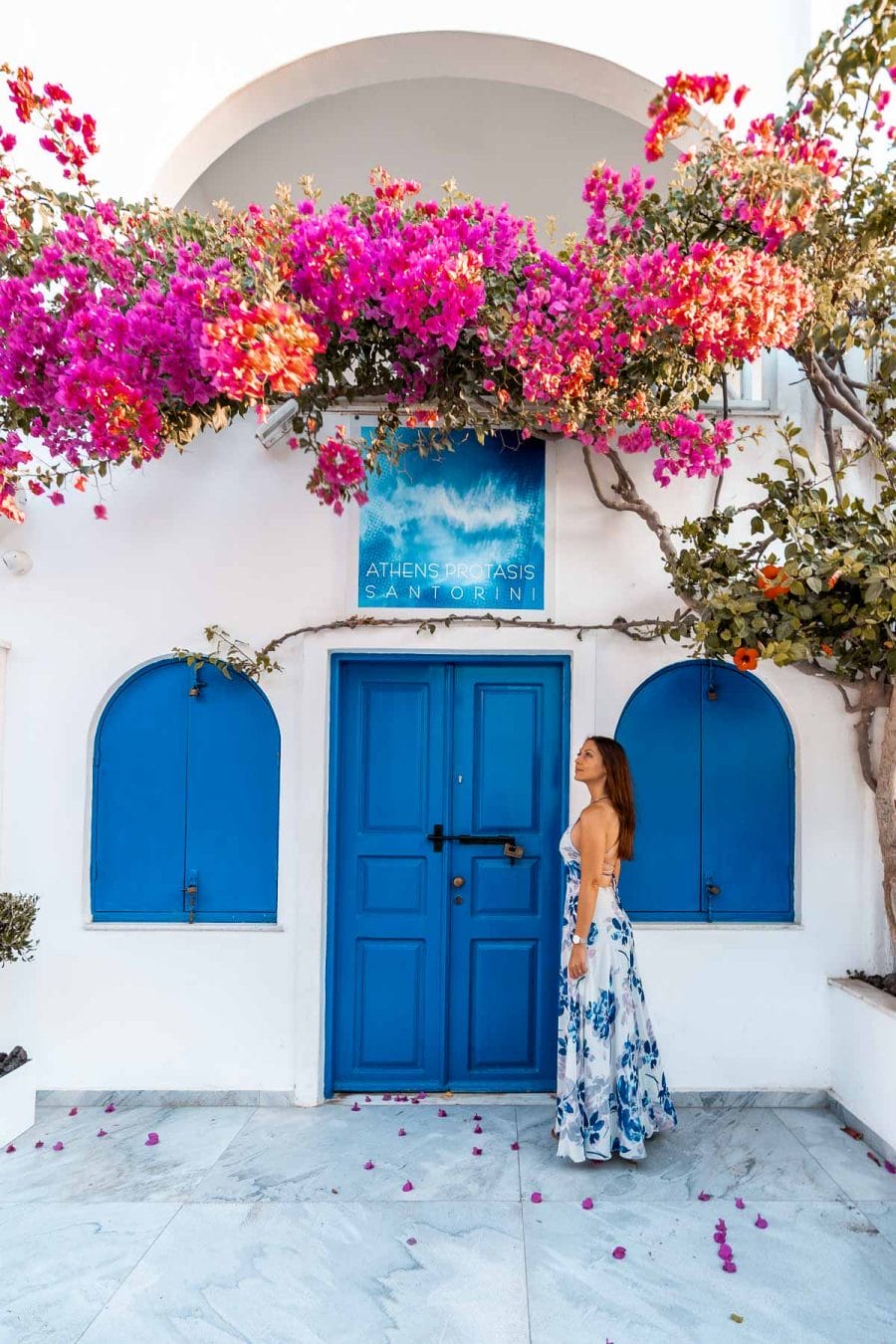 Girl standing at a Blue door with pink flowers in Oia, Santorini