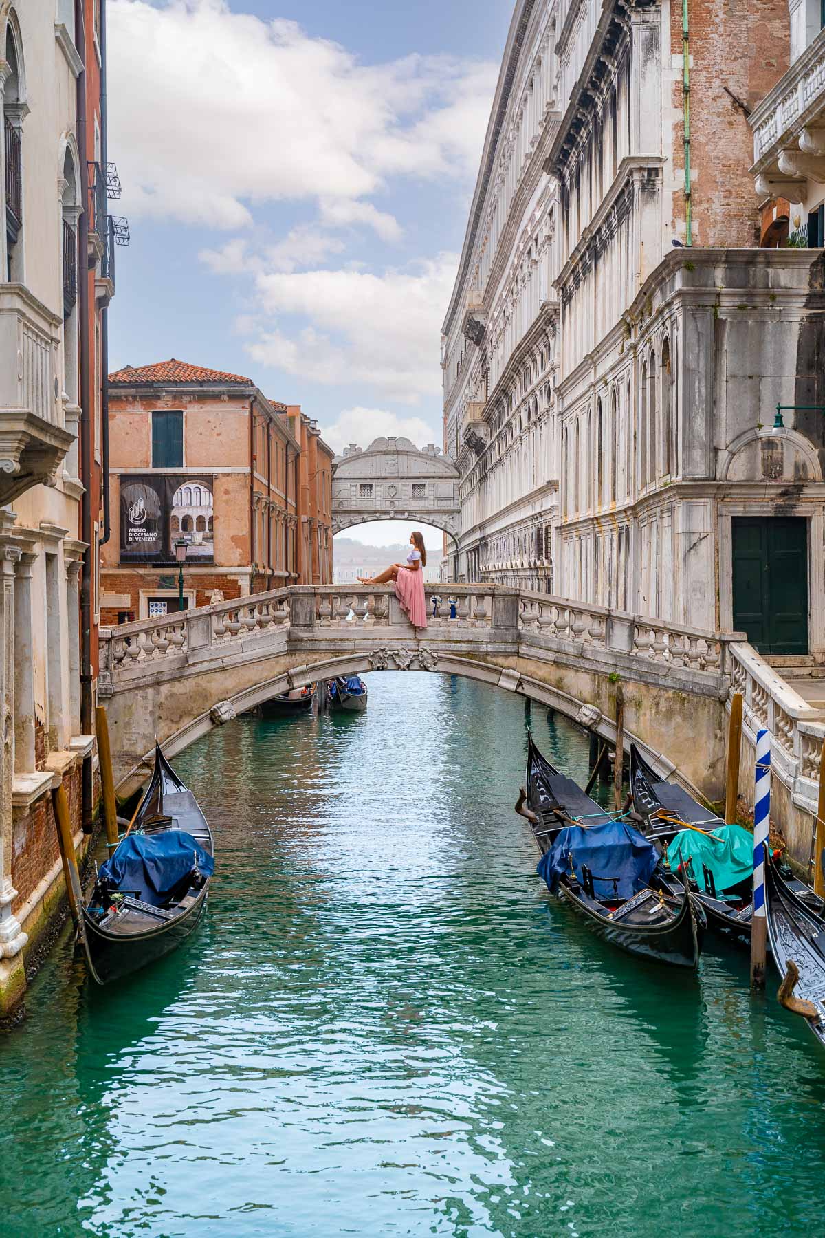 Girl in a pink skirt sitting on a stone bridge in front of the Bridge of Sighs in Venice