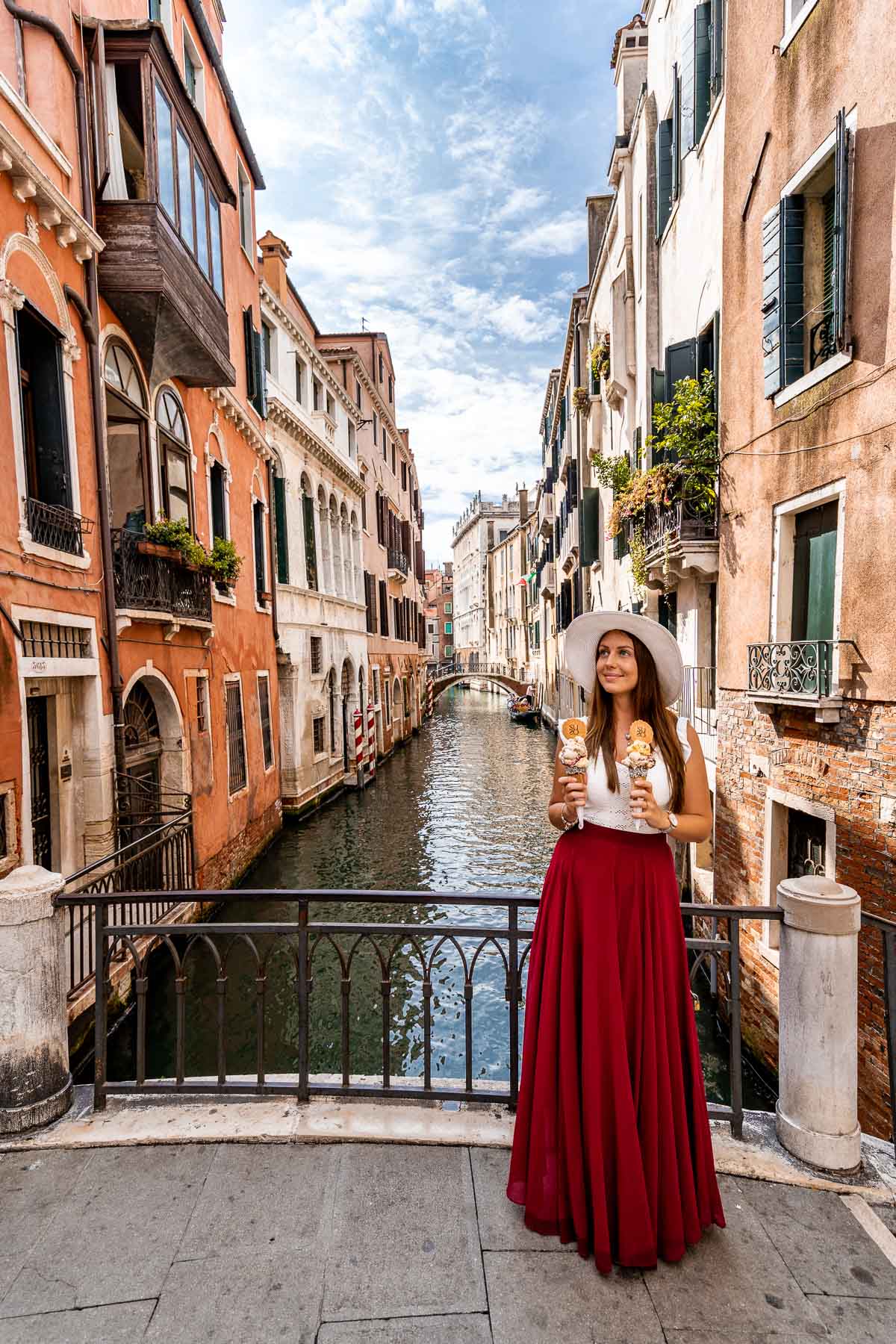 Girl in a red skirt standing on a bridge in Venice with gelatos on her hand