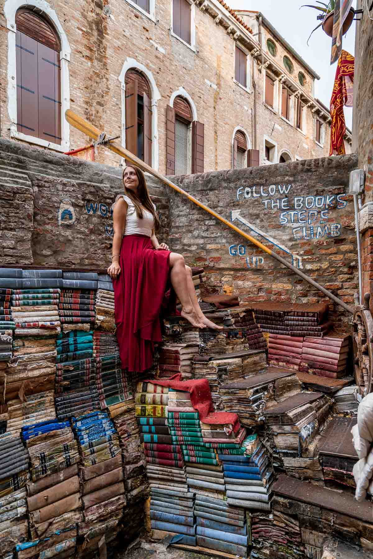 Girl in a red skirt sitting on top of the books at Libreria Acqua Alta in Venice, Italy