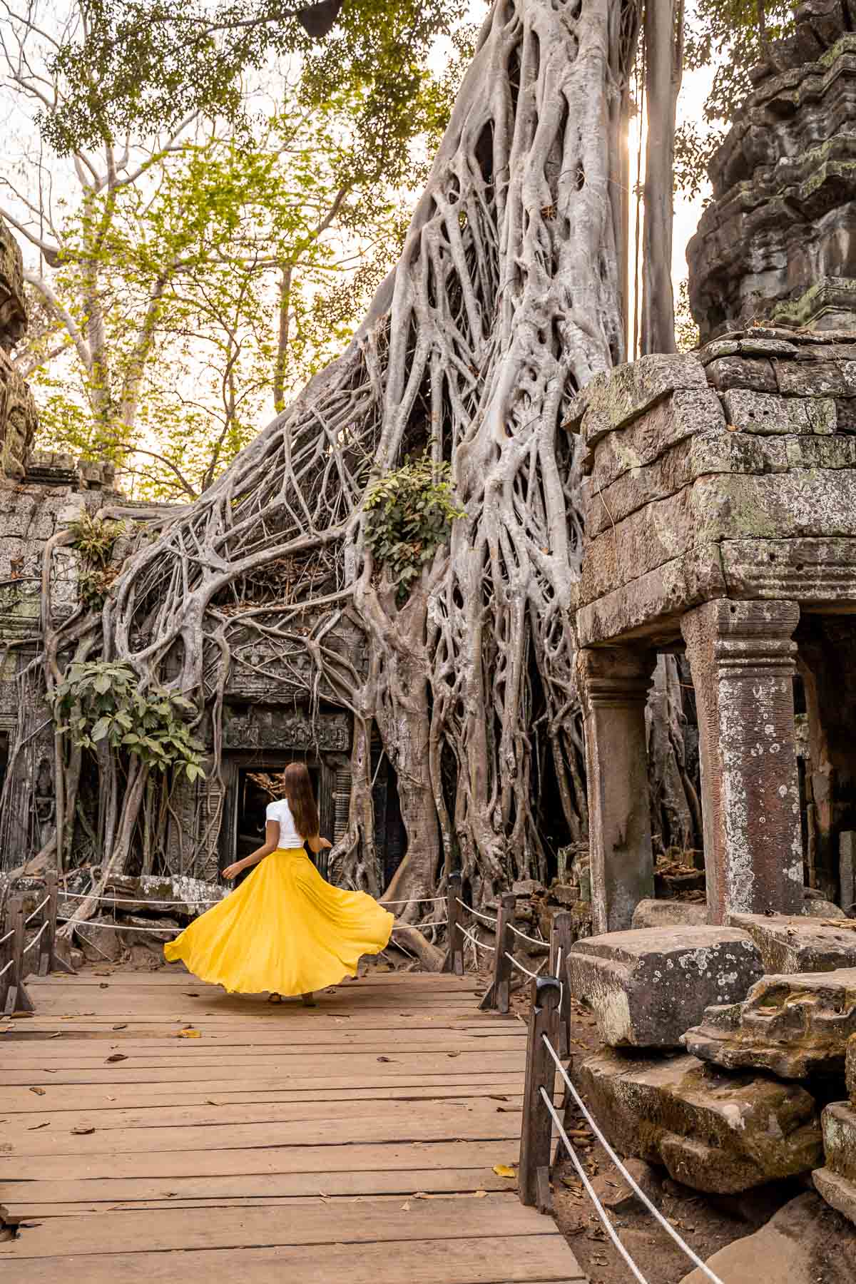 Girl in a yellow skirt twirling in Ta Prohm Temple in Cambodia