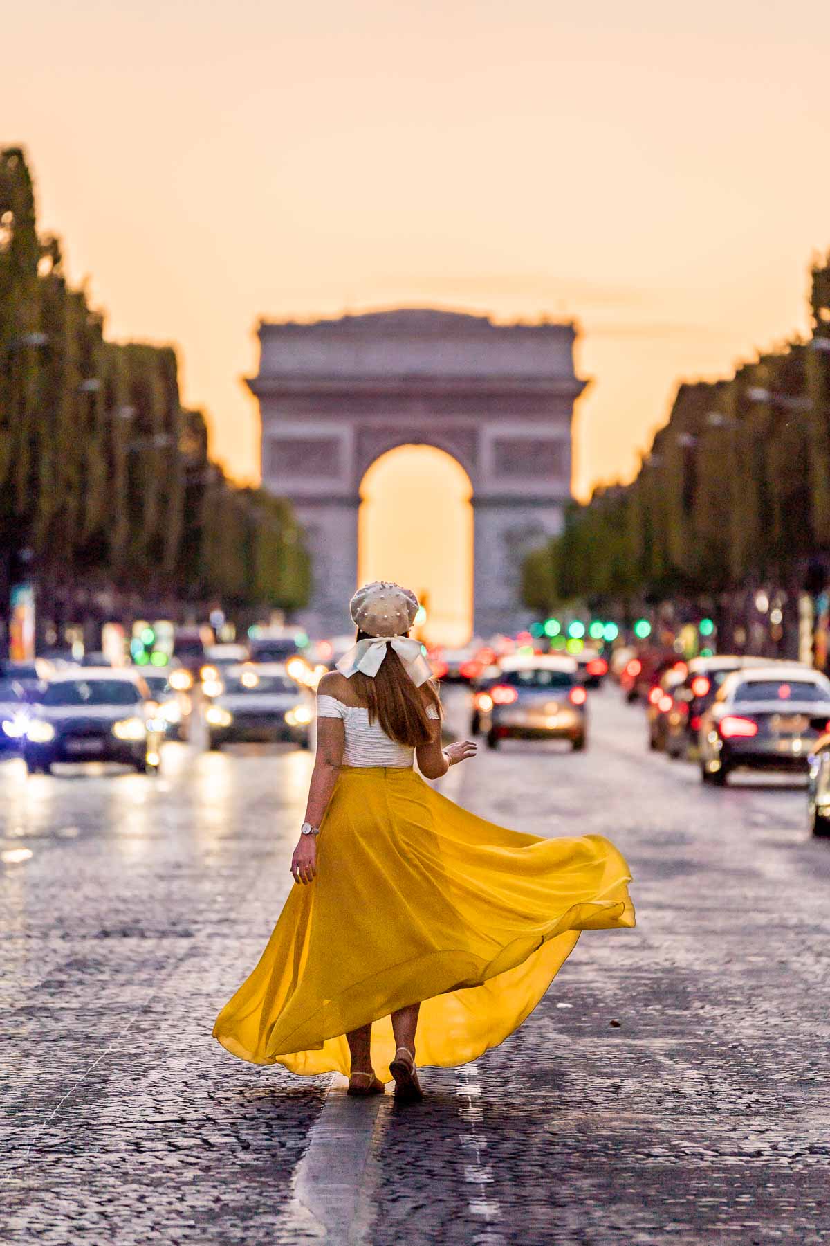 Girl in a yellow skirt standing in front of the Arc de Triomphe at the sunset