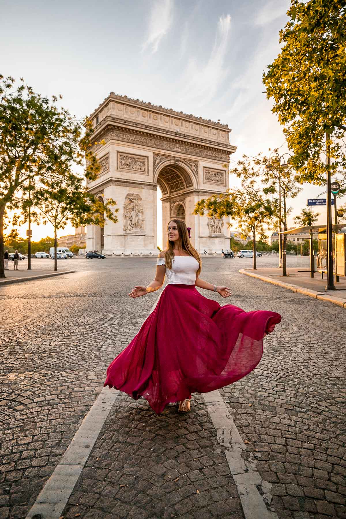Girl in a red skirt twirling in front of Arc de Triomphe, one of the best Paris Instagram Spots