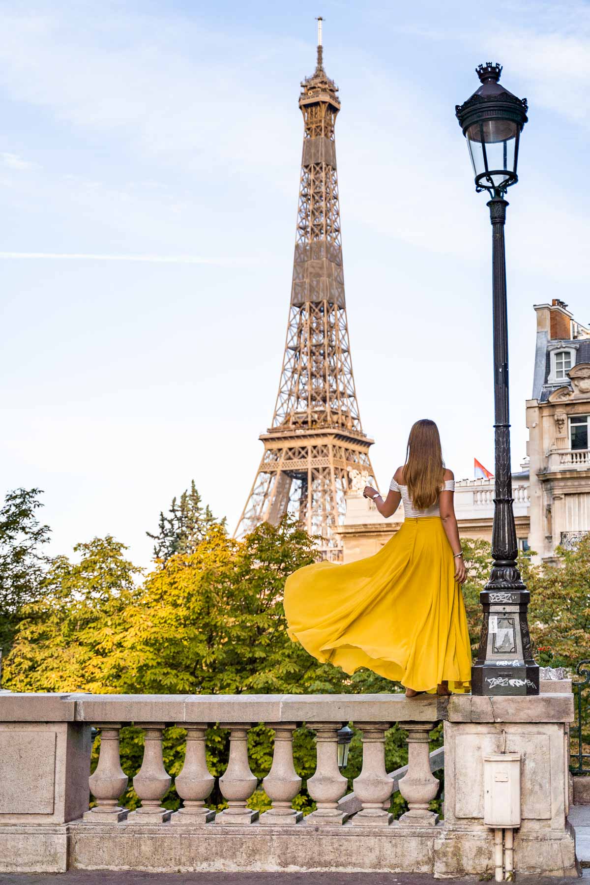 Girl in a yellow skirt twirling in front of the Eiffel Tower at Avenue de Camoens, Paris