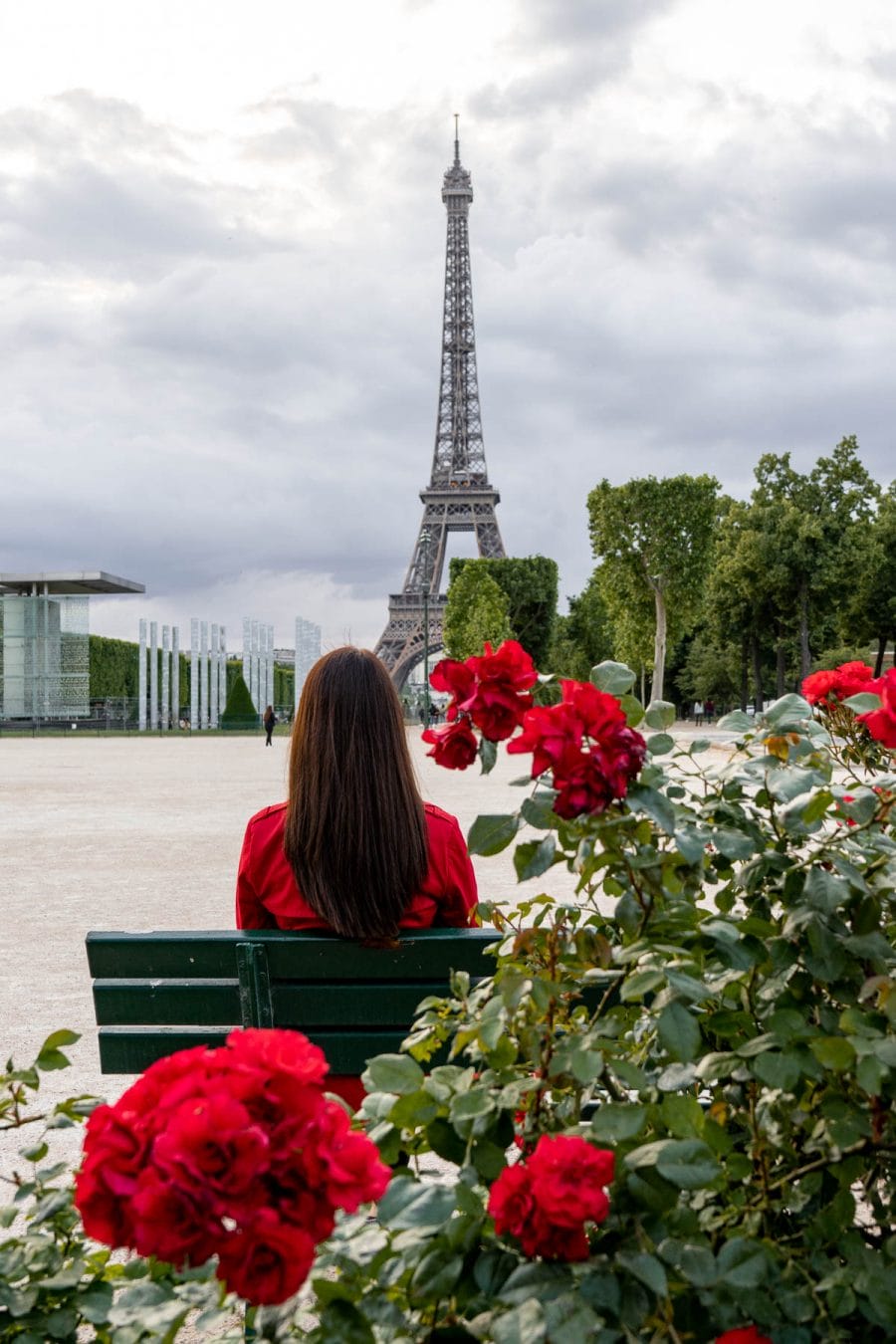 Girl in a red coat sitting on a bench, looking at the Eiffel Tower at Champ de Mars
