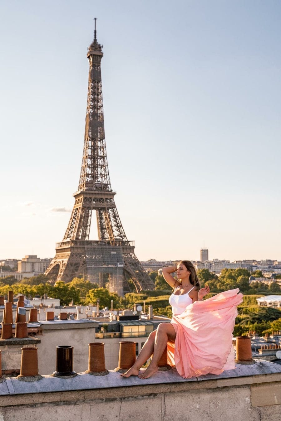 Girl in a pink skirt sitting on a rooftop in Paris with the Eiffel Tower in the background