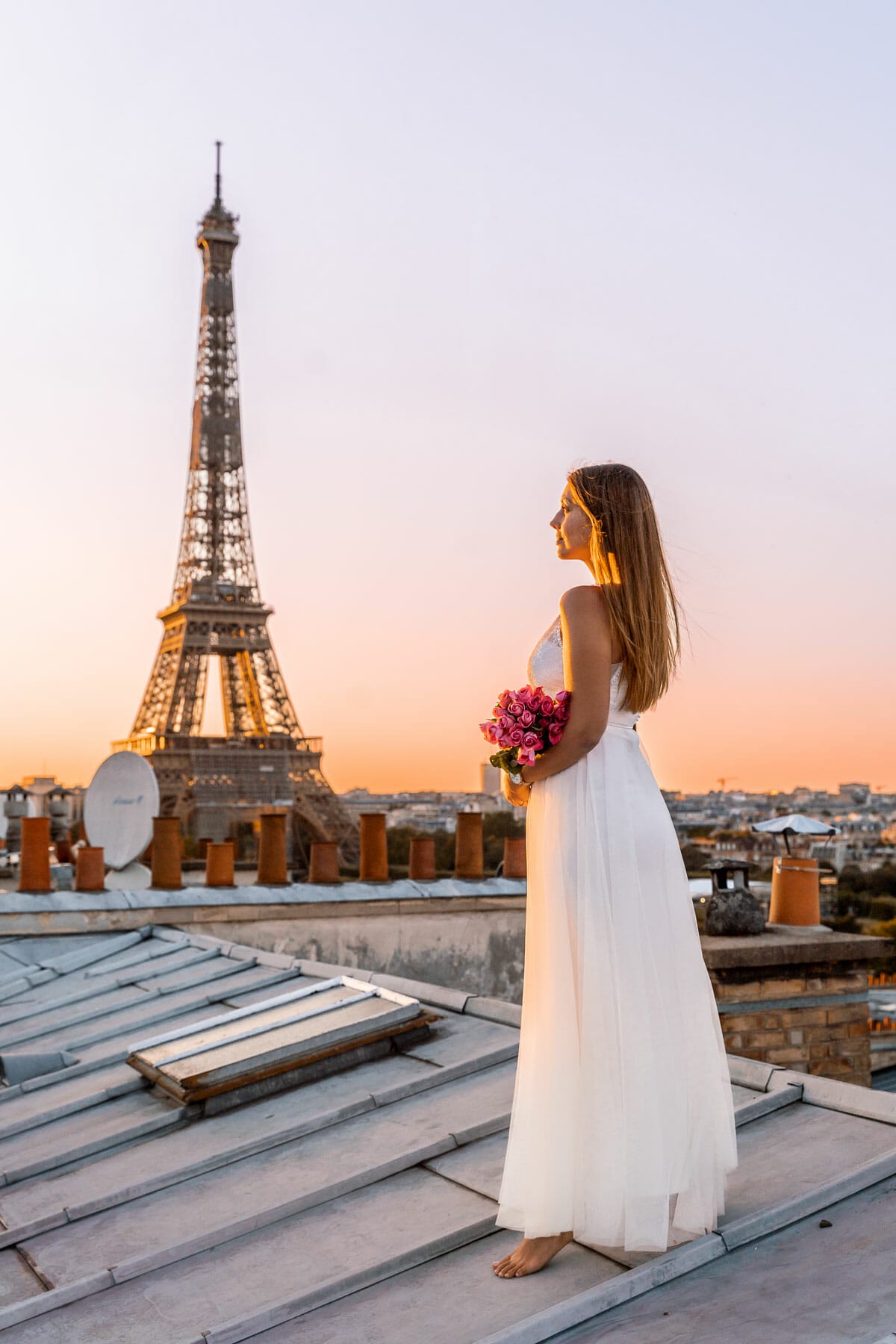 Girl in a white dress standing on a rooftop in Paris, looking at the Eiffel Tower