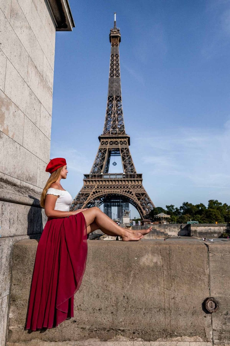 Girl in a red skirt and beret sitting on Pont d'Léna, looking at the Eiffel Tower