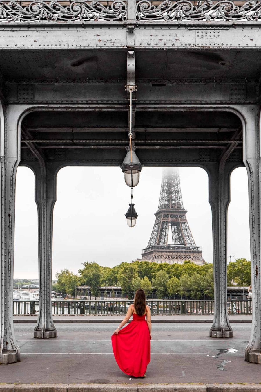 Girl in a red dress standing under Pont de bir-Hakeim, looking at the Eiffel Tower