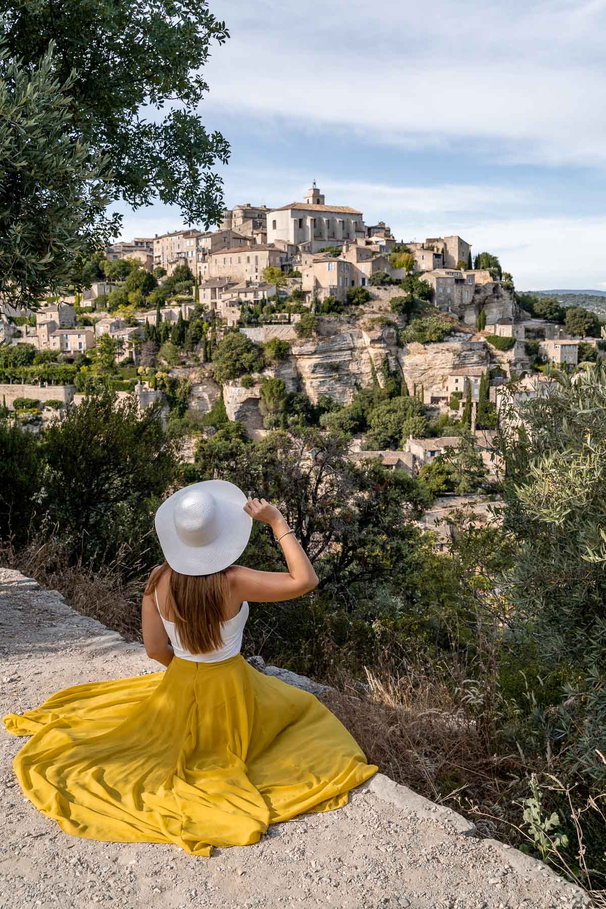 Girl in a yellow skirt sitting at a viewpoint, looking over the beautiful town of Gordes