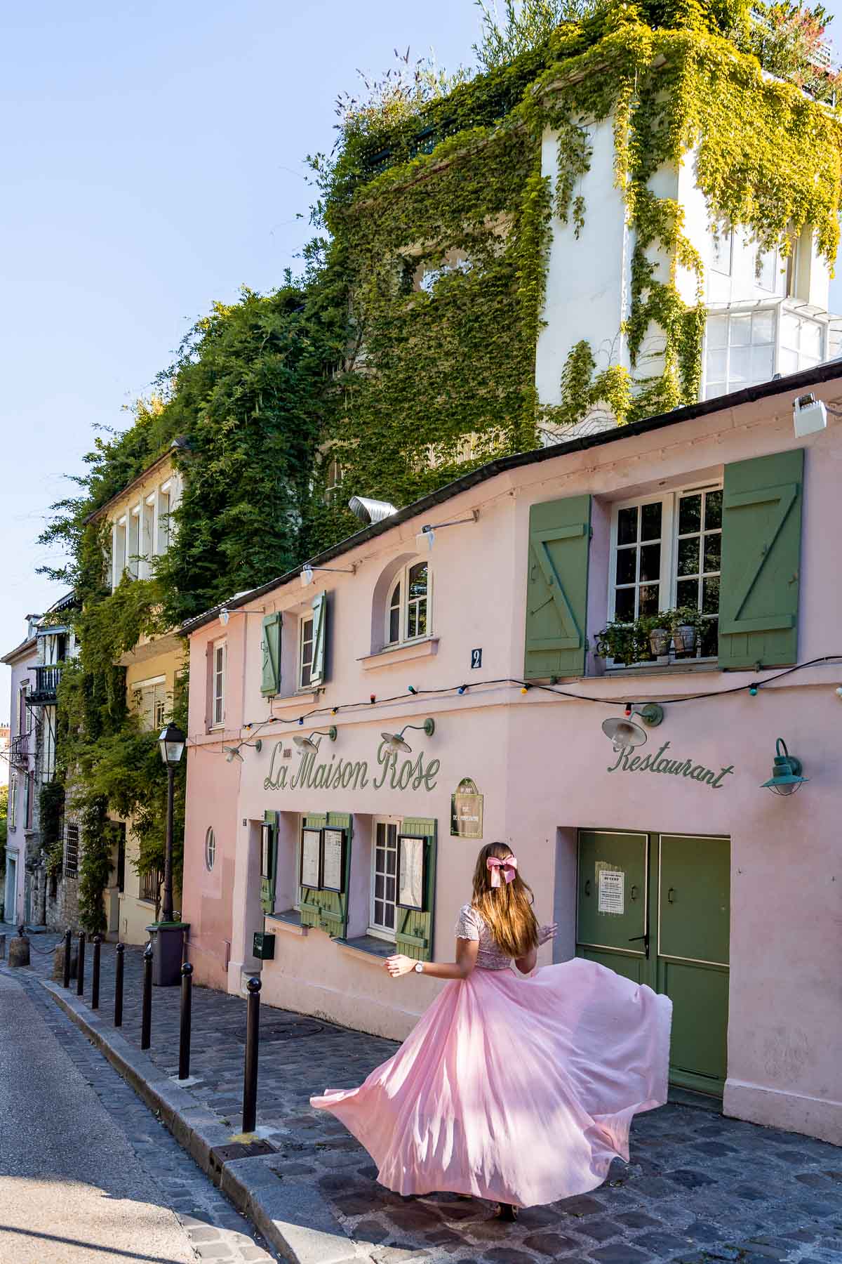 Girl in a pink skirt twirling in front of La Maison Rose in Montmartre, Paris
