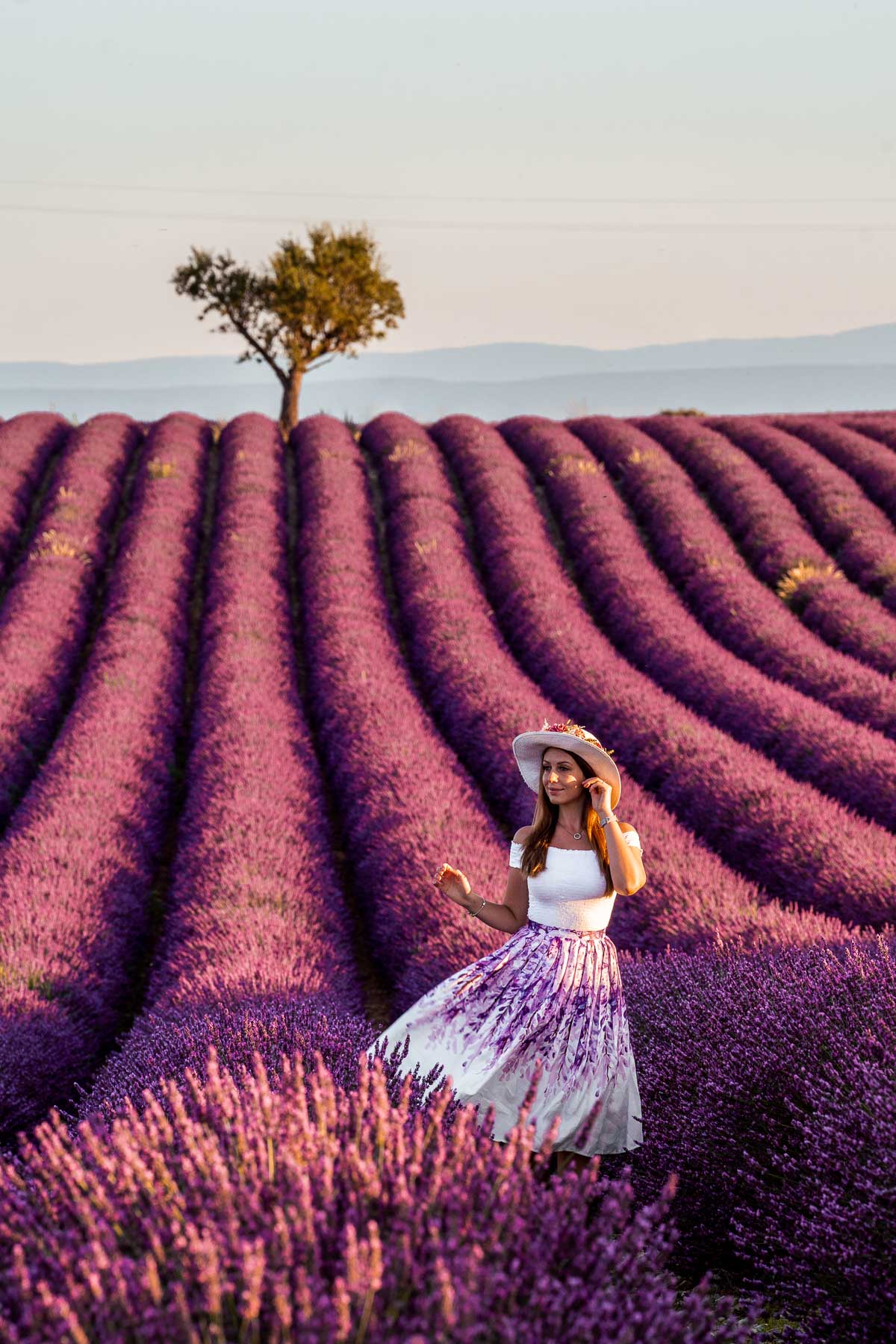 Girl in a purple skirt standing in the lavender fields with a heart shaped tree in the background in Provence