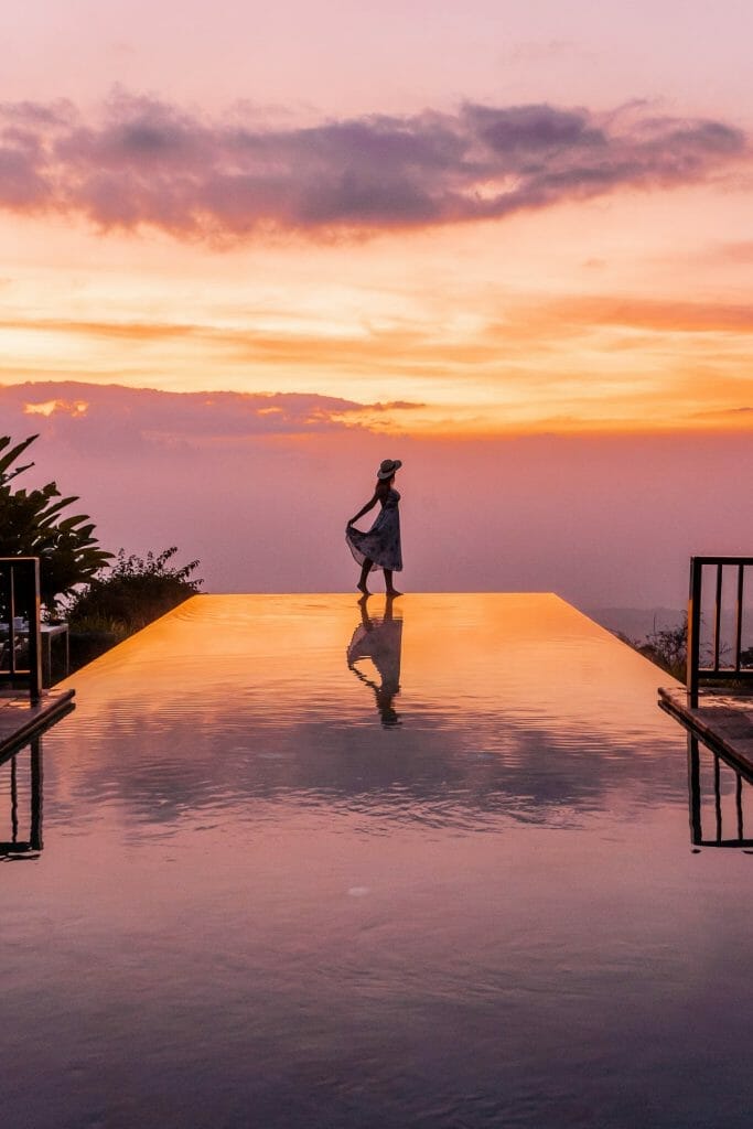 Girl standing on the edge of an infinity pool during sunset at Munduk Moding Plantation