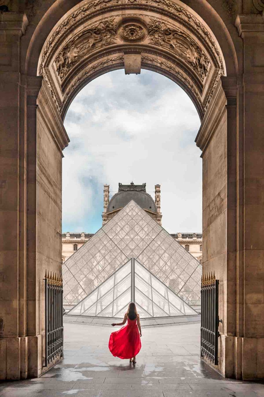 Girl in a red dress standing in front on the Louvre, one of the most instagrammable places in Paris