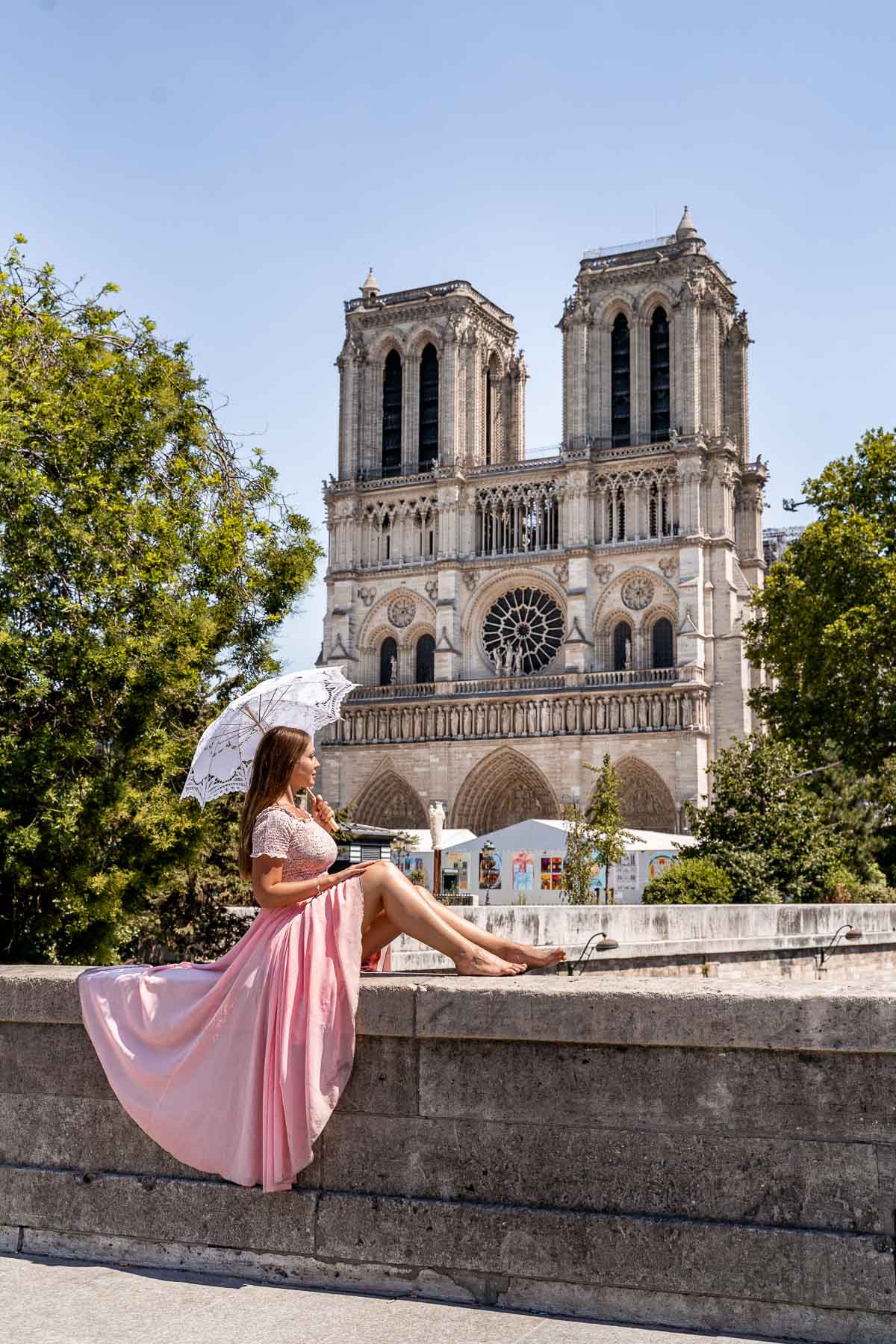 Girl in a pink skirt sitting in front of the Notre Dame, one of the most instagrammable places in Paris