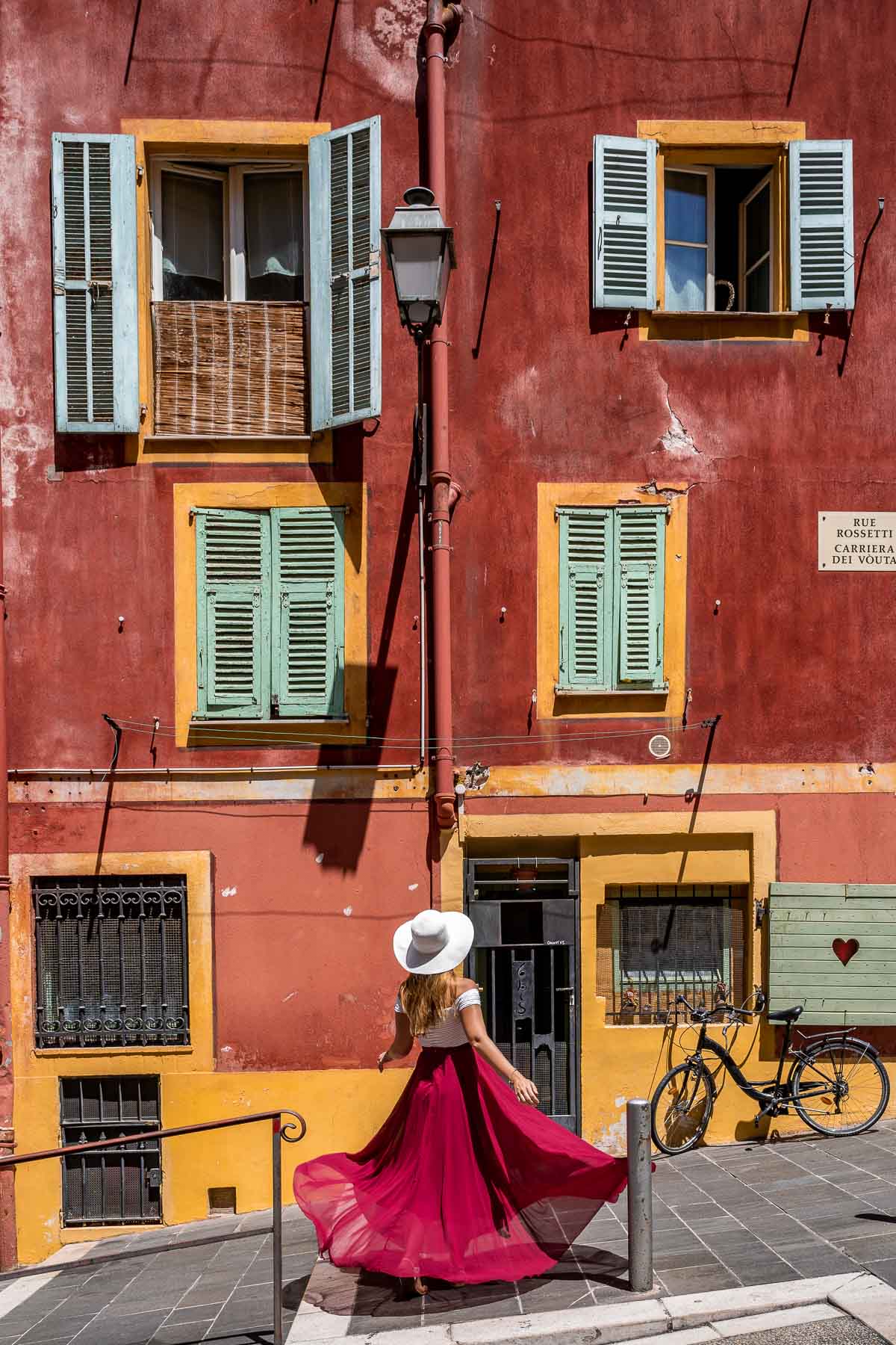 Girl in a red dress twirling in front of a colorful building in Nice, France