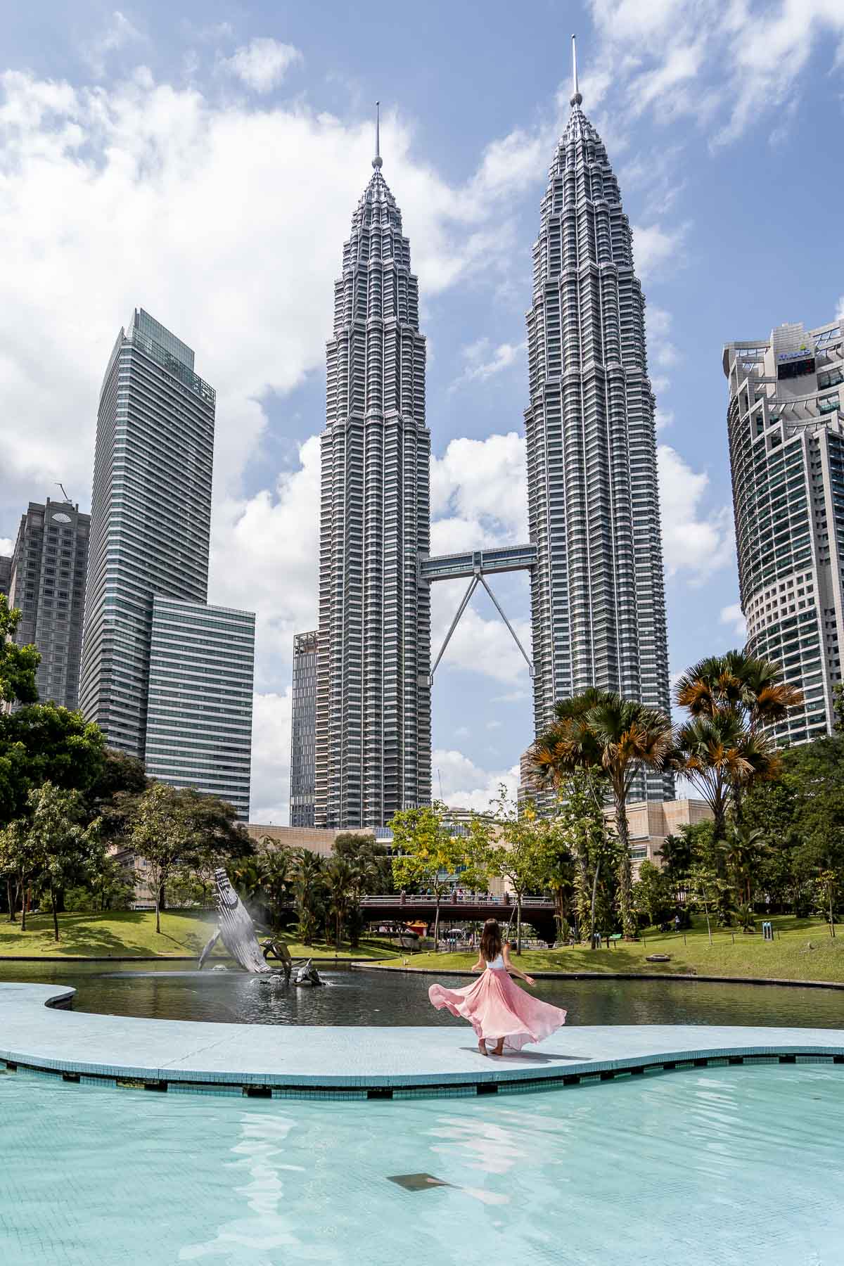Girl in a pink skirt twirling in front of the Petronas Towers in Kuala Lumpur