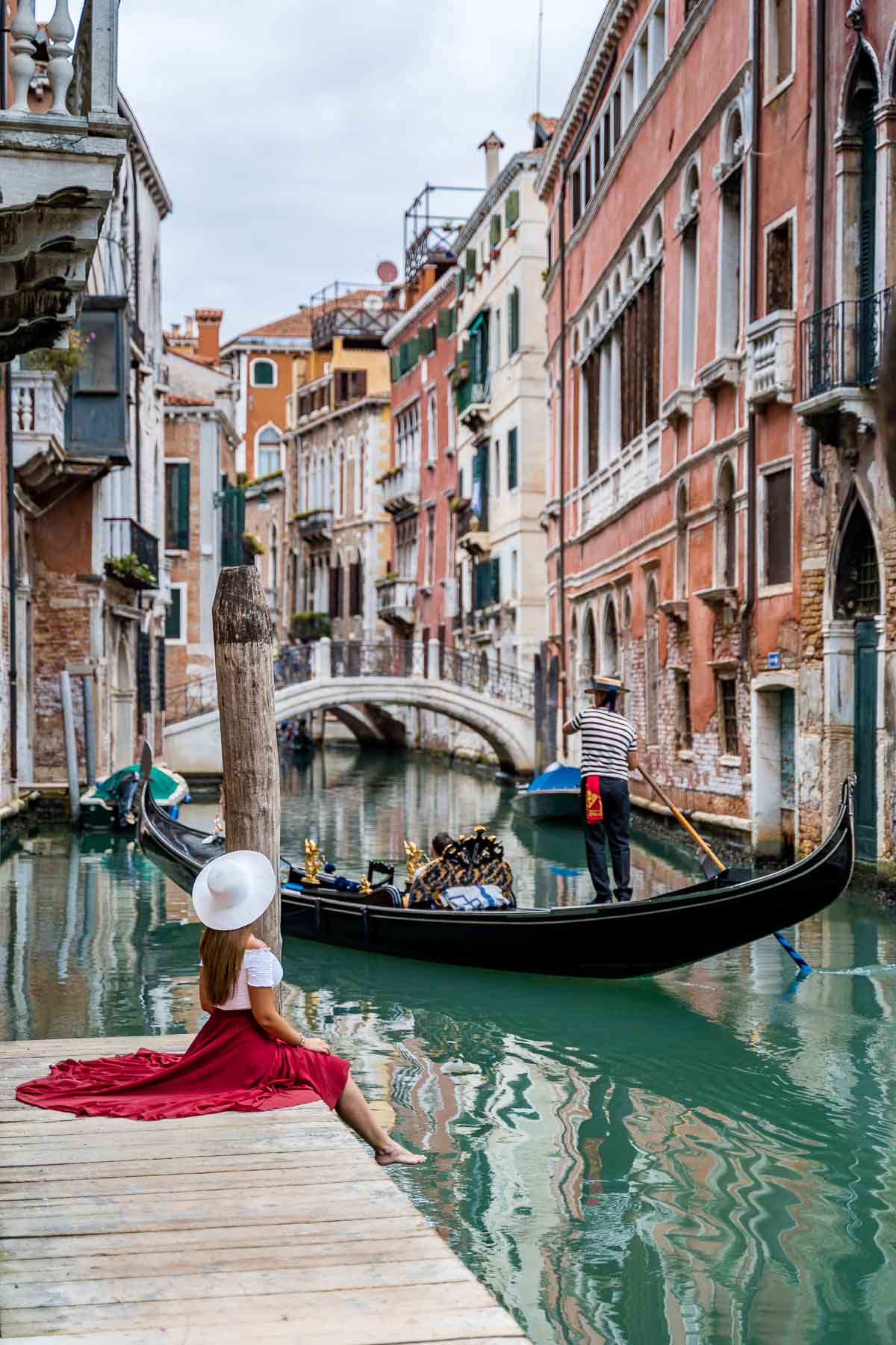 Girl in a red skirt sitting on a little pier along the canals, which is one of the best Venice Instagram spots