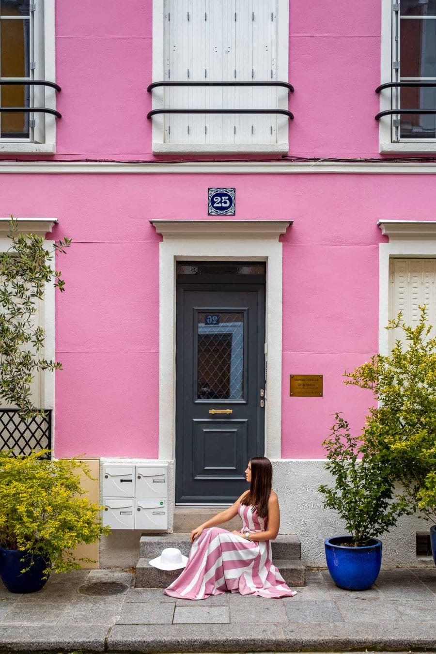 Girl in a pink-white dress sitting in front of a pink house at Rue Crémieux in Paris, France