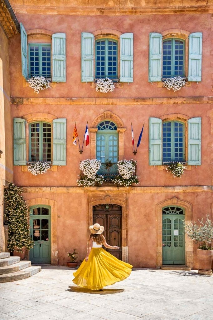 Girl in a yellow skirt twirling in front of the cute looking courthouse in Roussillon, Provence