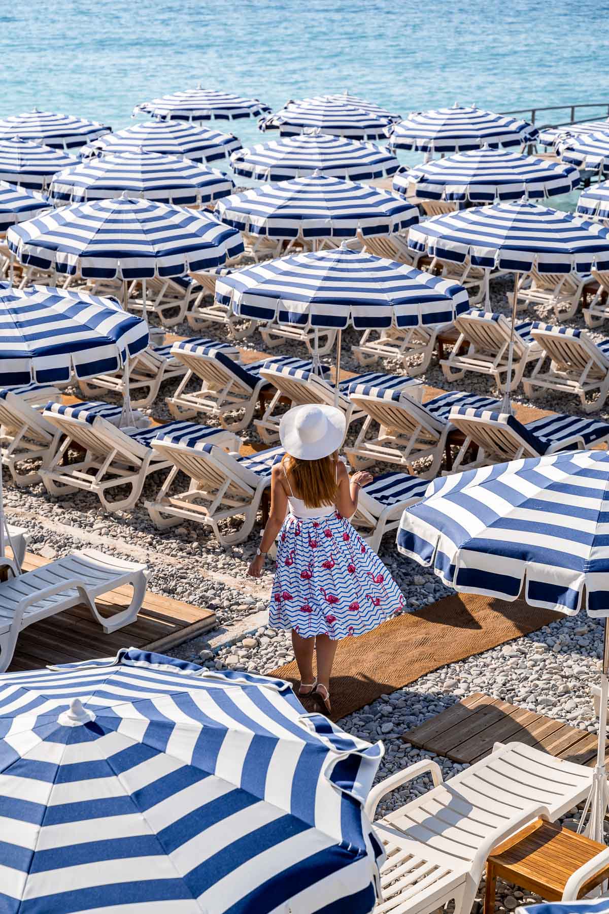 Girl in a flamingo skirt walking between the white-blue parasols at Ruhl Plage in Nice, France