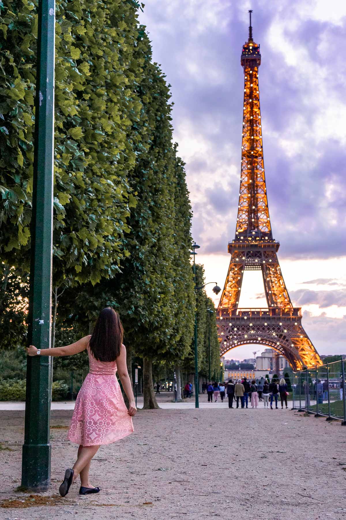 Girl in a pink dress watching the sparkling Eiffel Tower from Champ de Mars