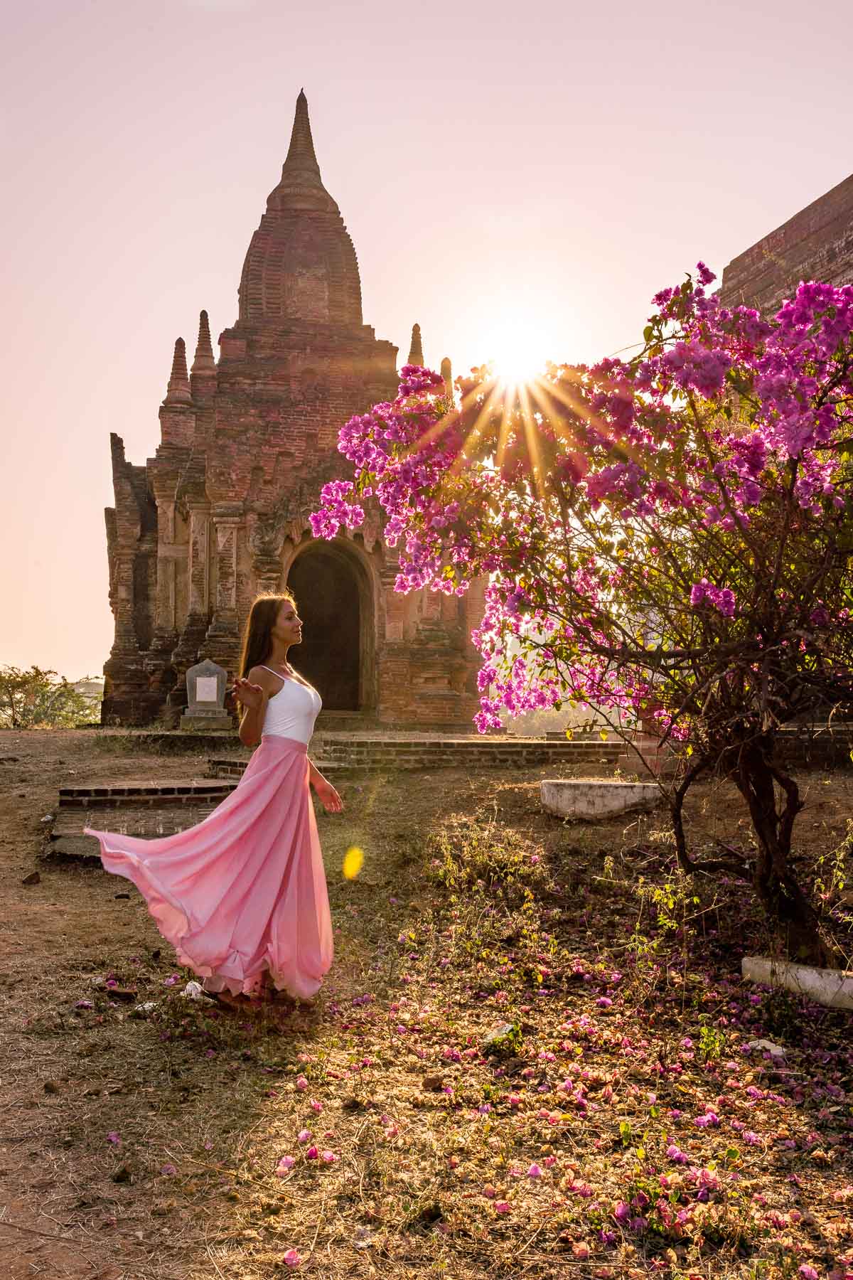 Girl in a pink dress watching the sunrise in front of a pink tree in Bagan, Myanmar