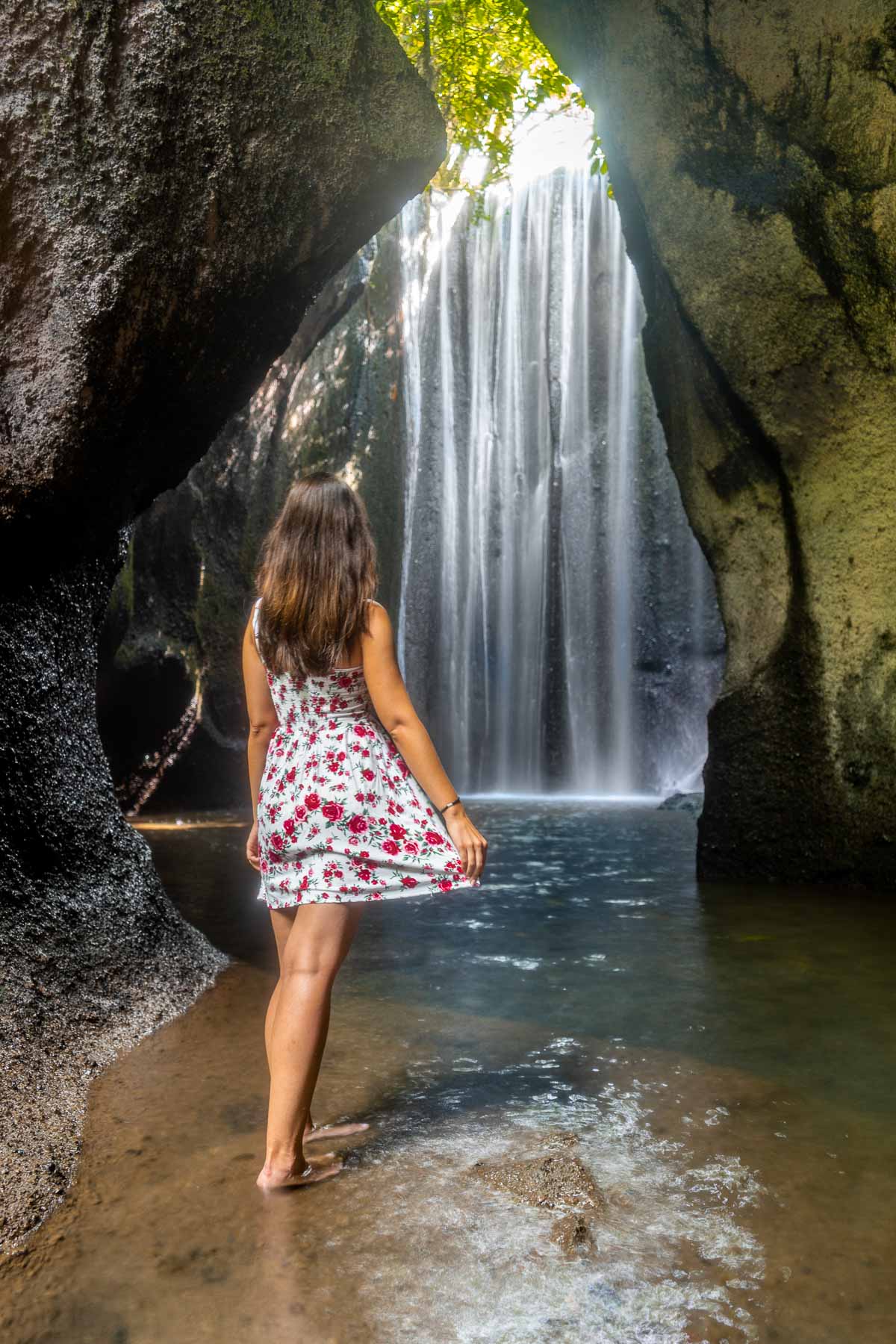 Girl in a red floral dress standing in front of Tukad Cepung Waterfall in Bali