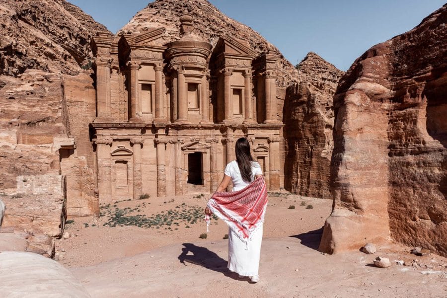 Girl in a white dress and a white-red keffiyeh standing in front of the Ad Deir Monastery in Petra, Jordan