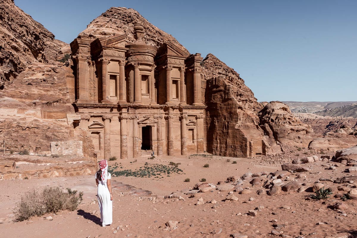 Girl in a white dress and a white-red keffiyeh standing in front of the Ad Deir Monastery in Petra, Jordan