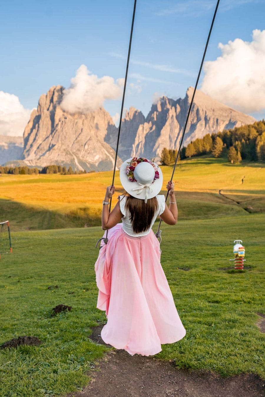 Girl in a pink skirt swinging at Alpe di Siusi in the Dolomites